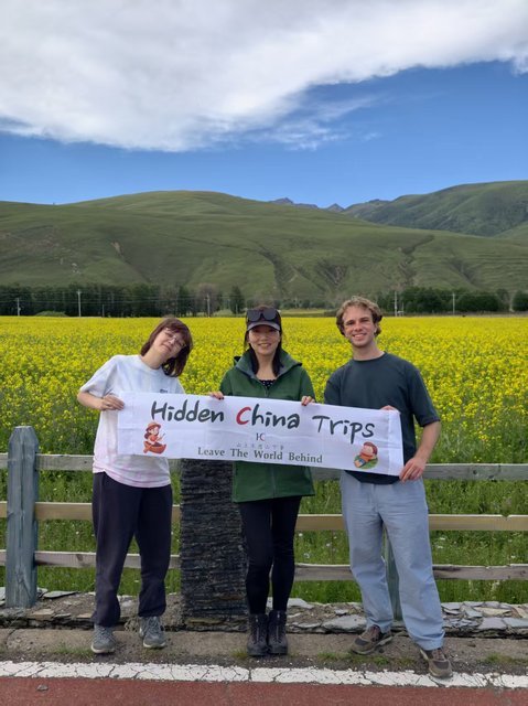 Travelers with Hidden China Trips banner in a canola field, Xinduqiao