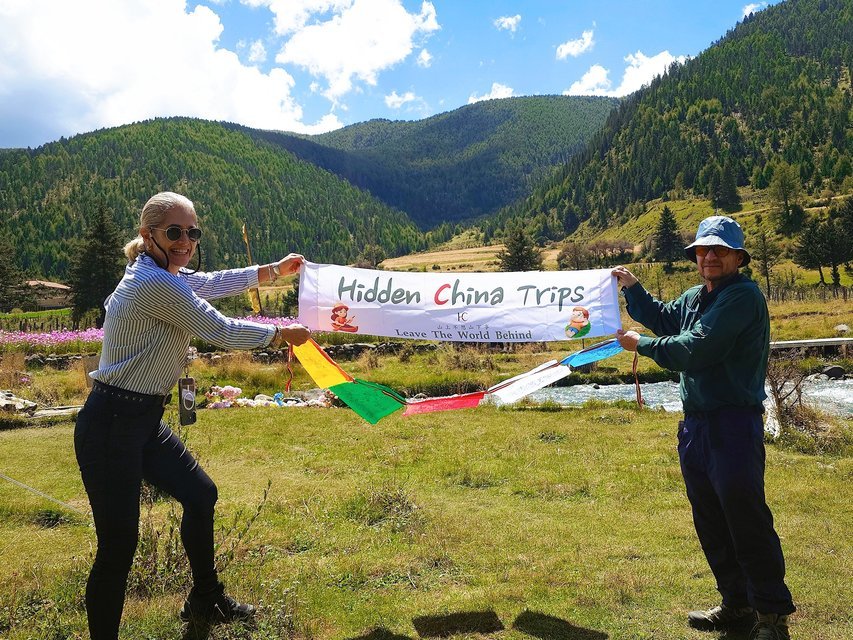 Travelers with Hidden China Trips banner and prayer flags, forest valley