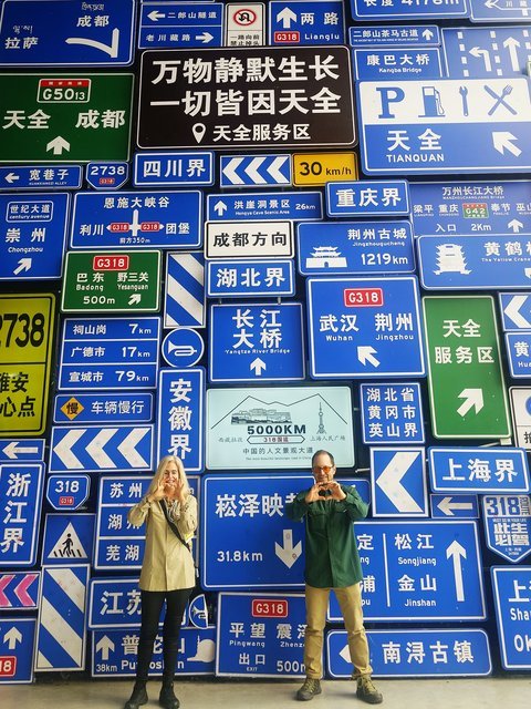 Travelers posing with a road-sign wall in Sichuan
