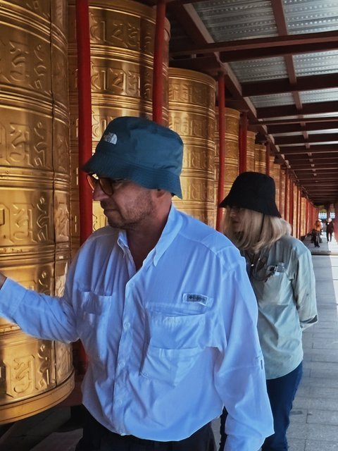 Travelers walking past golden prayer wheels