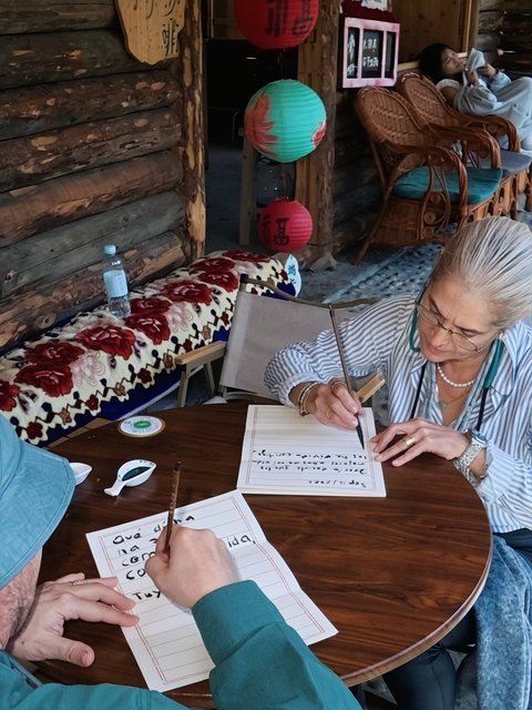 Travelers practicing calligraphy at a wooden table