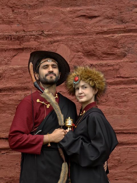 Couple in traditional Tibetan dress against a red rock wall