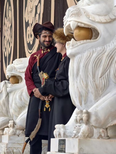 Couple in traditional Tibetan dress beside stone lion statues